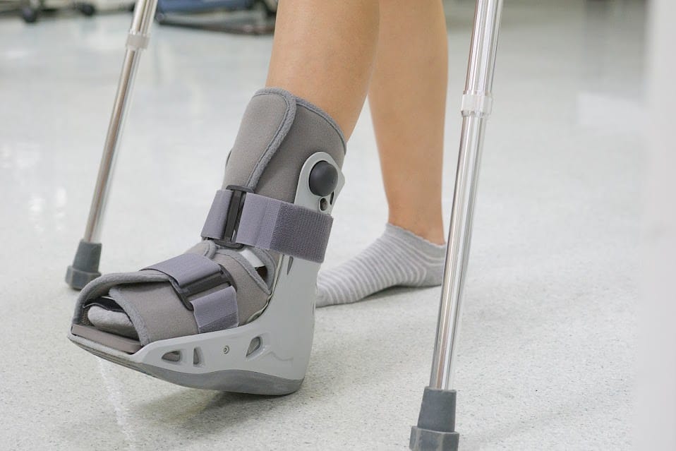 A person walking with crutches and a surgical boot